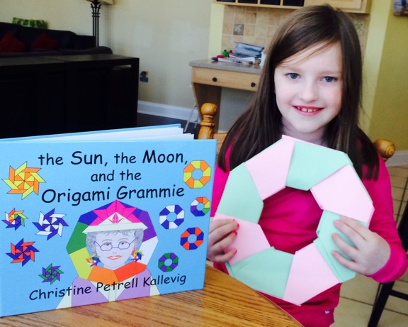 a girl holds up her own creation after reading the Sun, the Moon, and the Origami Grammie
